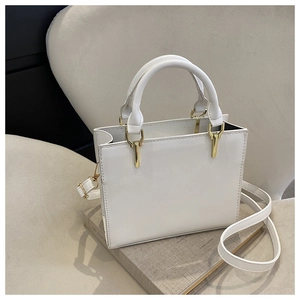 Detail of white minimalist square bag featuring gold metal bars and D-ring handle fixings