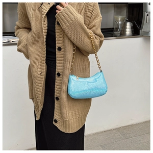 Dettaglio della borsa sottobraccio glitter blu chiaro con catena d'oro su cardigan