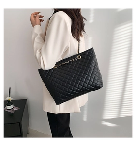Dettaglio della borsa tote nera in pelle trapuntata con catena dorata su modella elegante