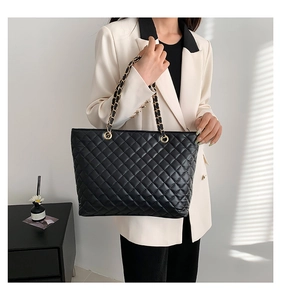 Detail shot of the black quilted tote bag featuring metallic chain straps and soft texture