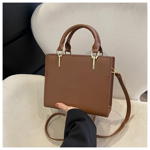 Detail of a brown leather handbag featuring stitching and golden cylindrical metal hardware