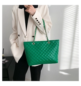 Dettaglio della borsa tote verde trapuntata con catena dorata su blazer bianco
