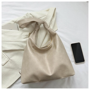 Detail of beige large capacity PU shoulder bag with unique knotted strap on white fabric