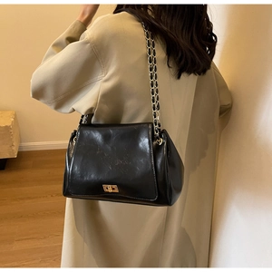 Detail of black glossy shoulder bag with gold twist lock and chain strap on trench coat