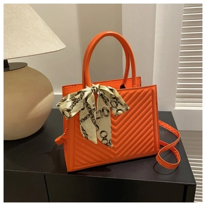 Détail d'un sac à main matelassé orange vif avec foulard en soie sur bois foncé