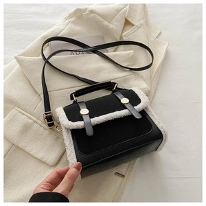 Detail of black leather handbag with white faux fur trim and gold buckles on a blazer