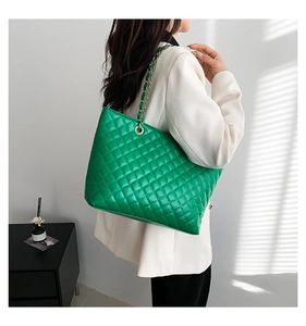 Dettaglio della borsa tote trapuntata verde con catena dorata sulla spalla della modella