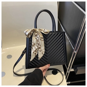 Détail macro d'un sac à main noir matelassé en V avec un foulard en soie décoratif au manche
