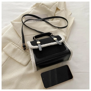 Detail shot of black leather handbag with white faux shearling trim and gold buckle