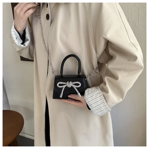 Close-up of black patent mini crossbody bag featuring a sparkling rhinestone bow detail