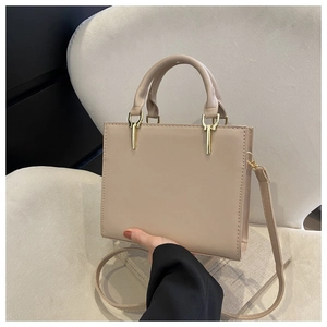 Detail of a beige matte leather handbag with dual handles and gold hardware on a chair