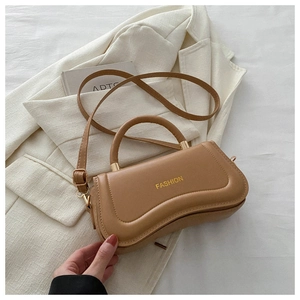 Close-up of a crescent-shaped tan leather handbag with gold hardware on a white blazer