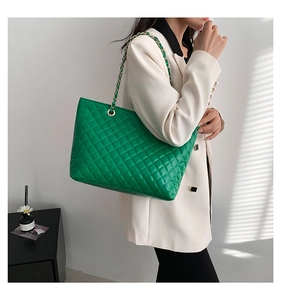 Close-up of green quilted tote bag featuring a leather-woven chain strap and soft texture