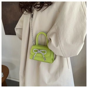 Detail of neon green mini crossbody bag with rhinestone bow and silver chain strap