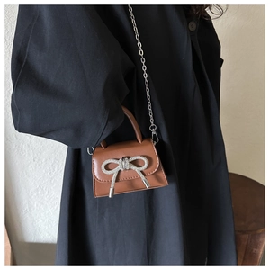 Detail of a brown mini crossbody bag with a rhinestone bow and elegant silver chain strap