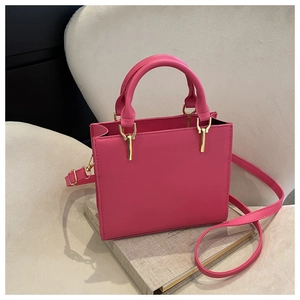 Detail view of pink stitch crossbody bag with golden hardware and top handle on books