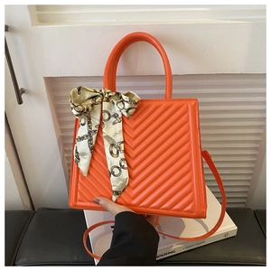 Détail du sac à main matelassé orange avec foulard en soie décoratif sur la poignée