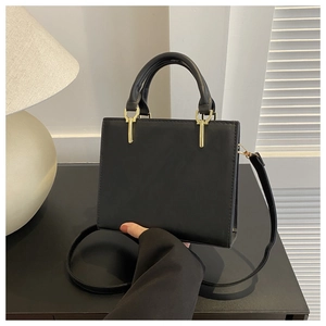 Close-up of minimalist black square handbag showing fine stitching and gold-tone hardware