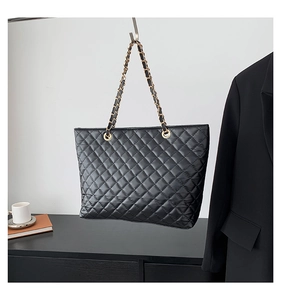 Detail of black quilted tote bag with gold chain strap next to a blazer and coffee