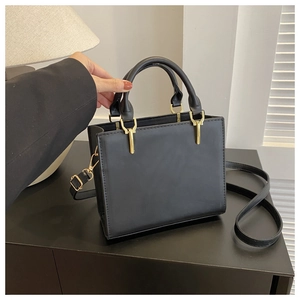 Detailed close-up of a black square leather bag with golden hardware and sewing line
