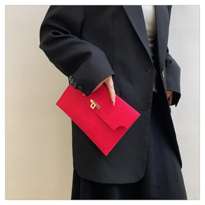 Detail of red crocodile embossed envelope clutch with iconic gold turn-lock closure