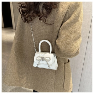 Close-up of white mini handbag with sparkling rhinestone bow and silver chain strap