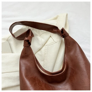 Deep brown faux leather shoulder bag with unique knot detail on the strap over a blazer