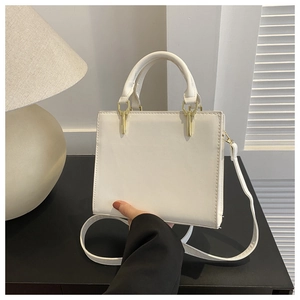 Close-up of cream-white leather handbag featuring gold U-shaped metal handle connectors