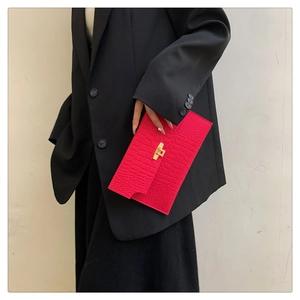 Detail of red crocodile texture envelope clutch bag with gold clasp on black outfit
