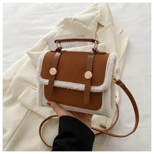 Detail of brown leather and white faux shearling bag with gold buckles on a white blazer