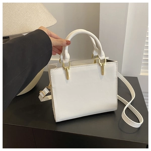 Detail showing white faux leather bag with golden hardware and round top handle