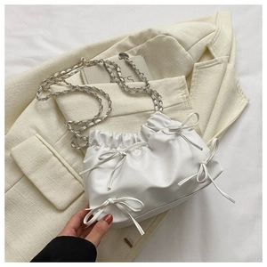 Detail of white pleated bucket bag with bows and silver chain on a beige blazer