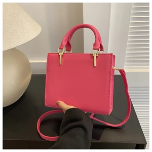 Detail view of fuchsia leather square handbag with golden hardware and adjustable strap