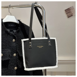 Detail of contrast lamb wool trim on black tote bag with gold logo and shoulder strap