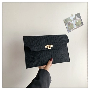 Close-up of black envelope clutch bag featuring crocodile texture and golden metal lock