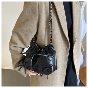Detail of black leather bucket bag with ribbon bows and silver chain strap on coat
