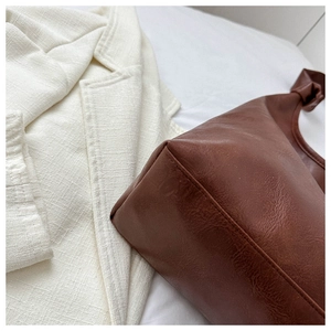 Close-up of dark brown PU leather tote bag with unique knotted handle detail on white blazer
