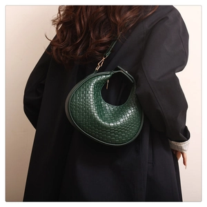 Close-up of deep green woven leather crescent bag paired with a classic black coat