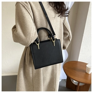 Detail of a black matte leather square handbag with gold hardware and sewing stitches