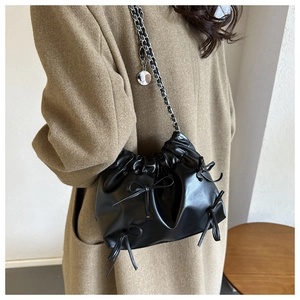 Detail of black pleated bucket bag featuring ribbon bows and silver chain strap