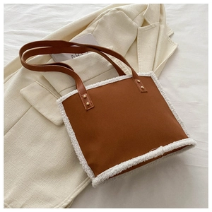 Close-up of brown faux leather tote bag featuring white shearling trim and gold rivets