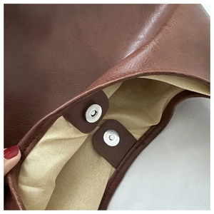 Close-up of brown PU leather bag showing silver magnetic closure and beige fabric lining