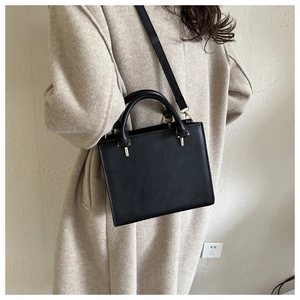 Detailed view of a black crossbody bag styled with a beige wool coat for a chic winter look