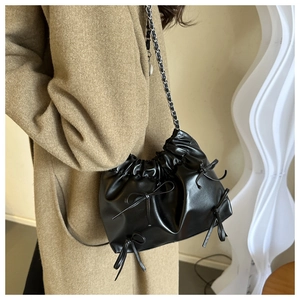 Detail of black drawstring bucket bag with bow accents and woven chain strap on model