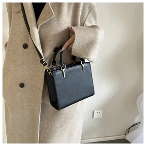 Detail of a minimalist black PU leather handbag worn over a beige wool coat for women