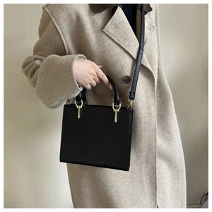 Detail of a matte black square crossbody bag with gold metal hardware and stitched texture