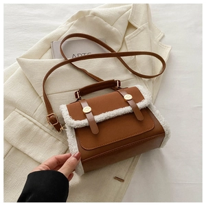 Detail of brown faux leather crossbody bag with white plush trim and golden metal buckles