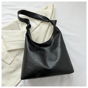 Detail view of large black PU leather tote bag with knotted strap on white blazer background
