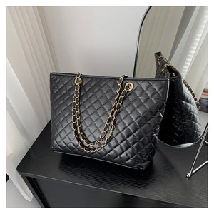 Quilted black tote bag with diamond texture and gold chain strap on a dark surface