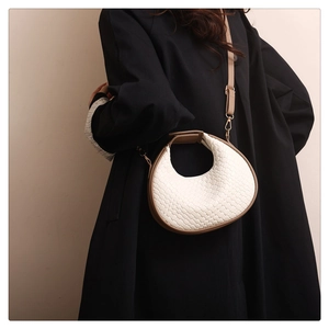 Detail view of a woven half-moon bag in cream and brown with gold metal hardware and strap